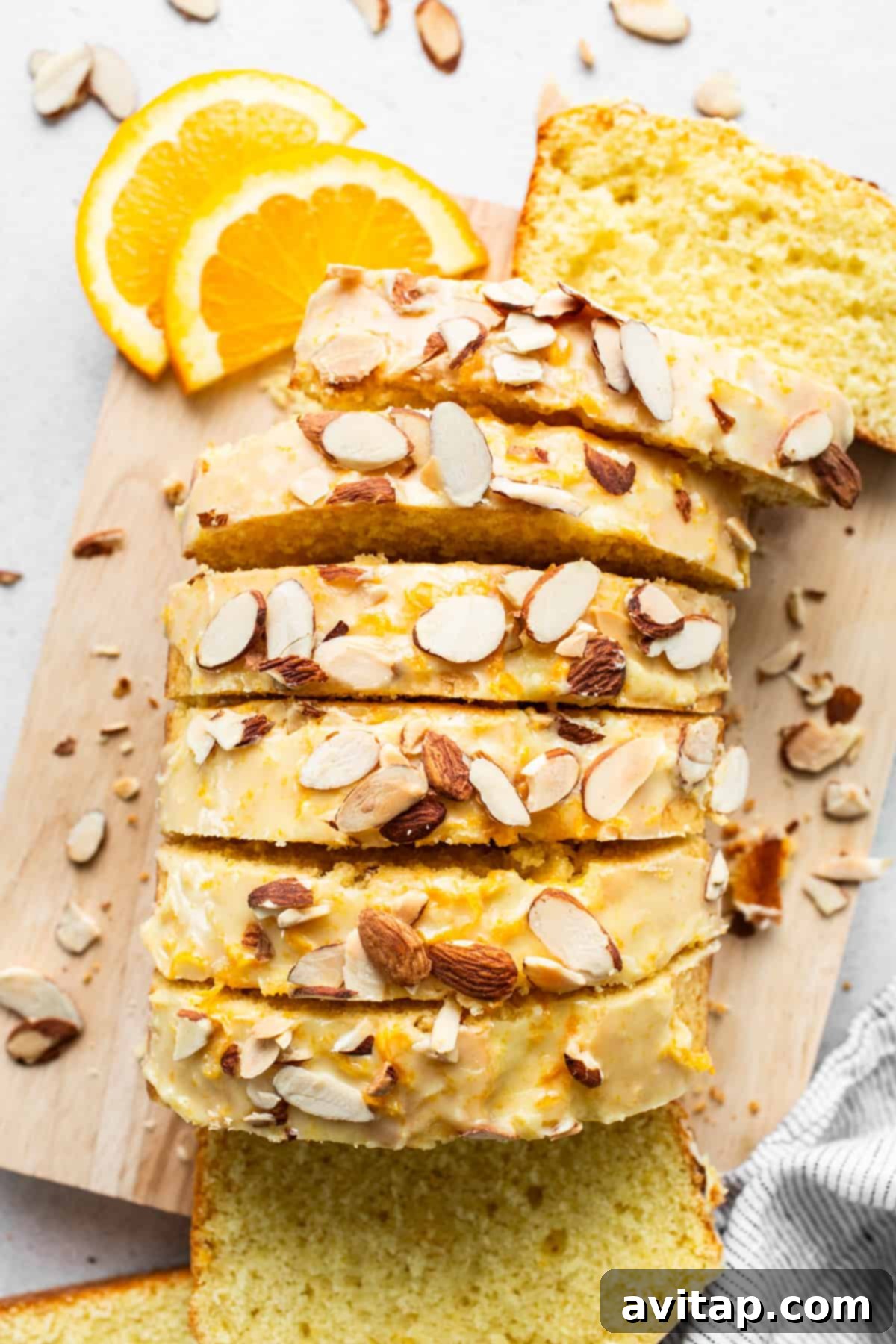 Zesty Orange Sunshine Cake 2 A beautifully sliced orange loaf cake with a glossy orange glaze and sprinkled with slivered almonds, resting on a wooden cutting board.