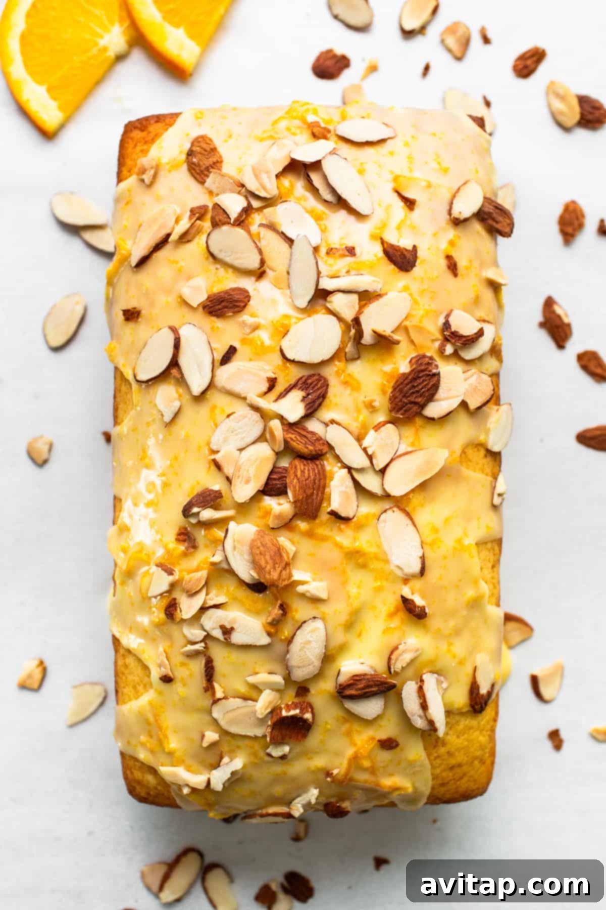 Zesty Orange Sunshine Cake 4 A beautifully decorated orange loaf cake, glazed and topped with slivered almonds and thin orange slices, on a light background.