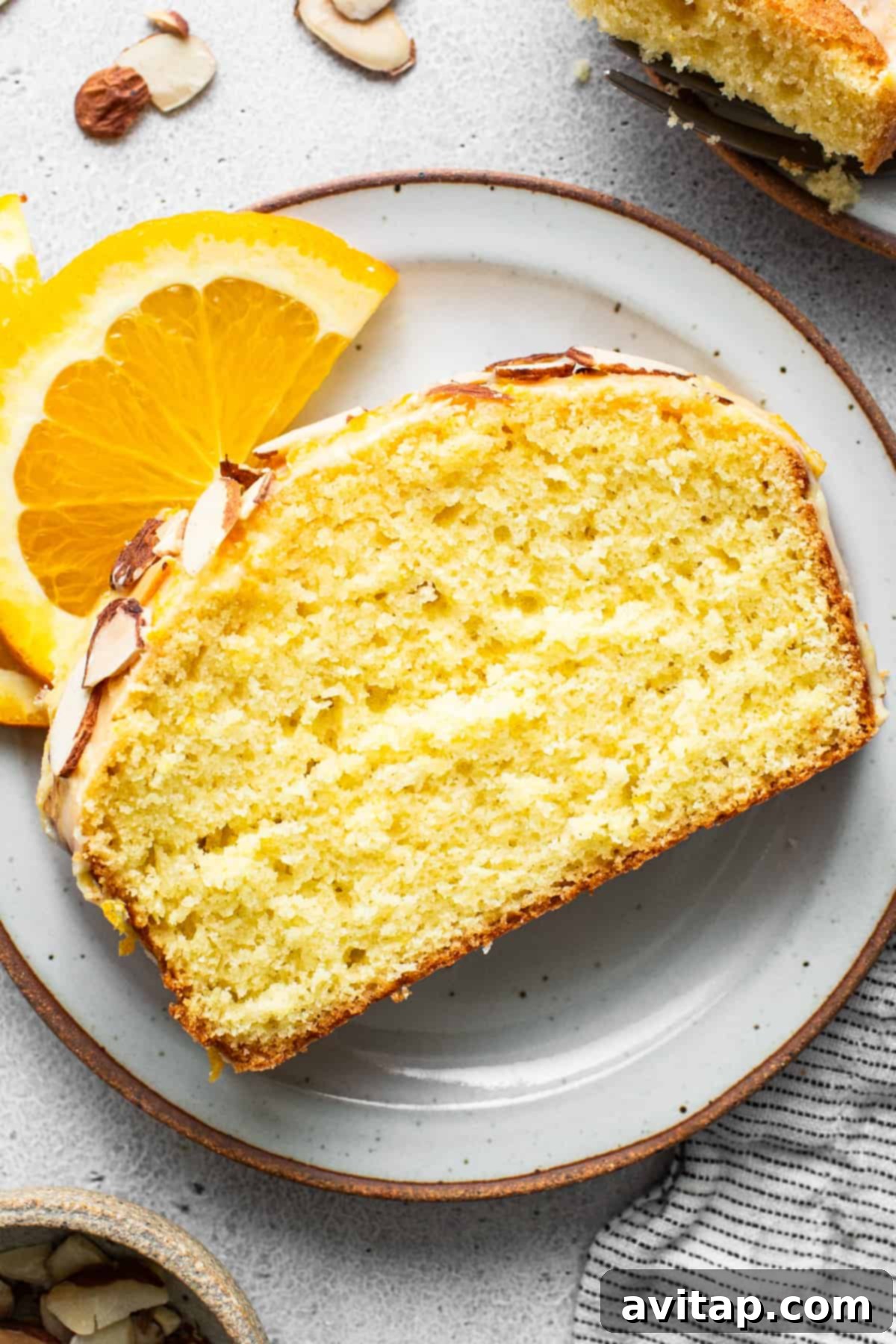 Zesty Orange Sunshine Cake 6 A generous slice of orange cake, adorned with a sweet glaze and slivered almonds, presented on a minimalist white plate.