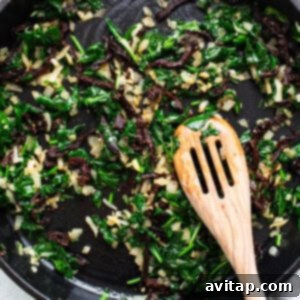 A skillet filled with greens and a wooden spoon.