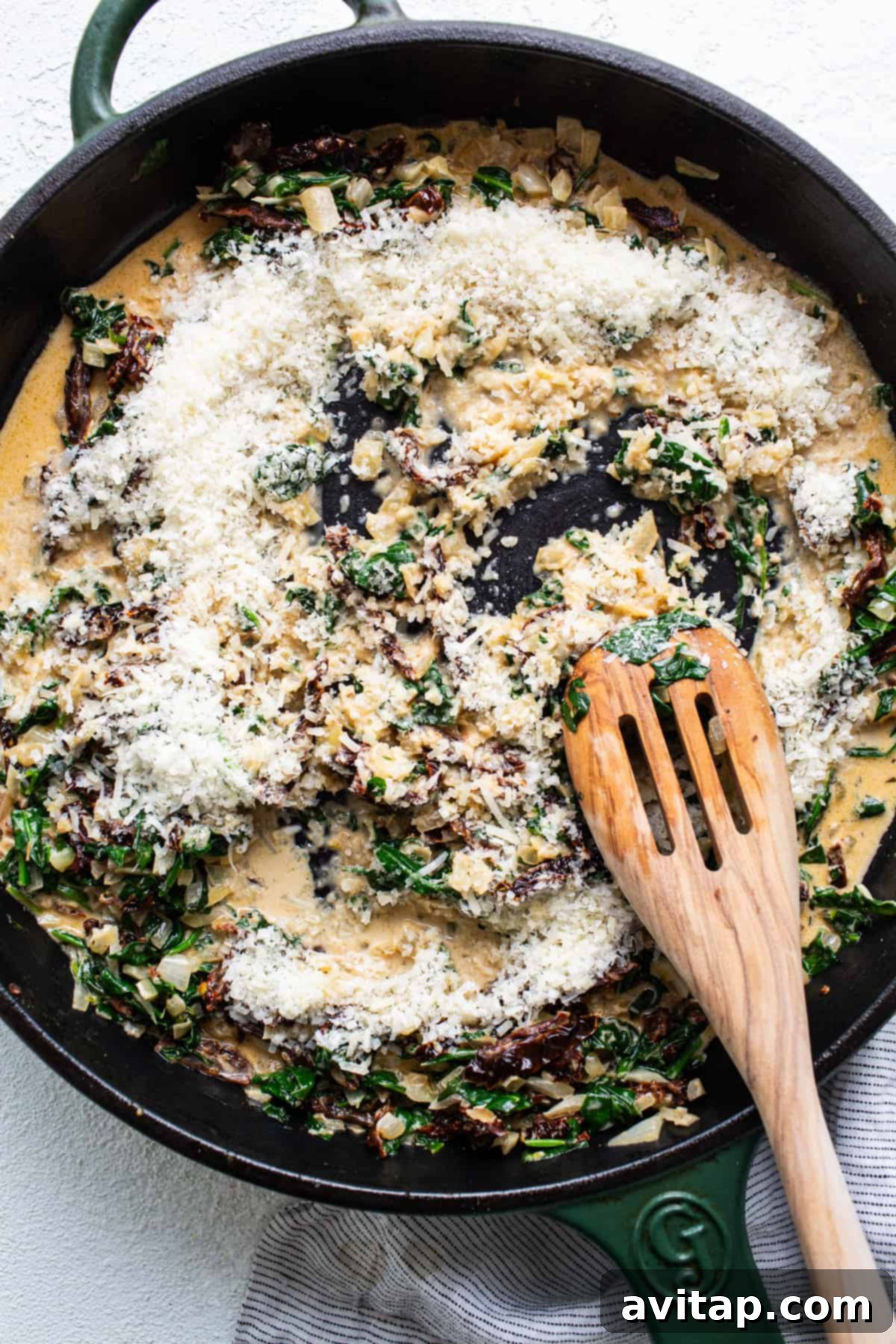 A skillet filled with spinach and cheese with a wooden spoon.