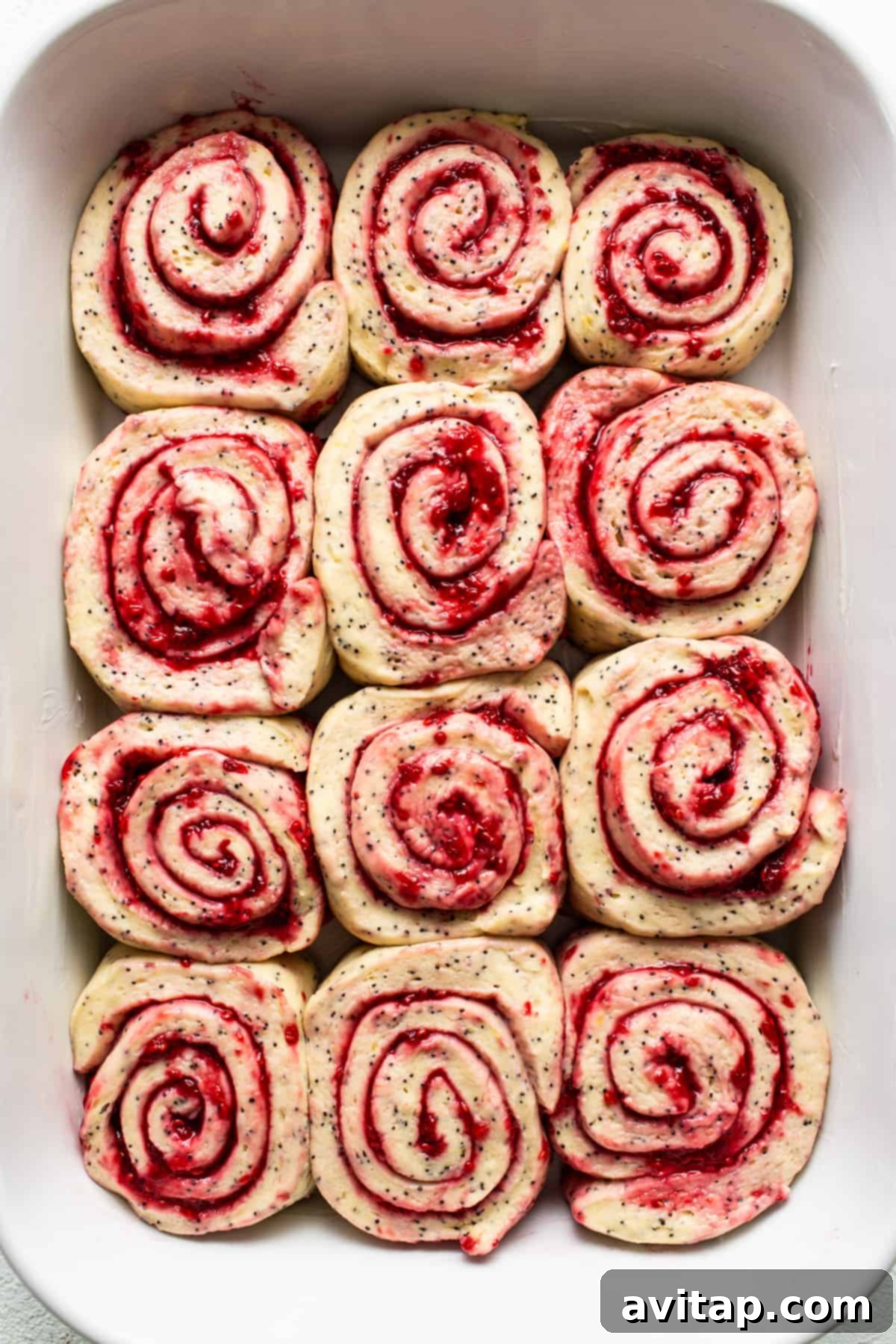 Raspberry roll ups arranged in a white baking dish before baking.