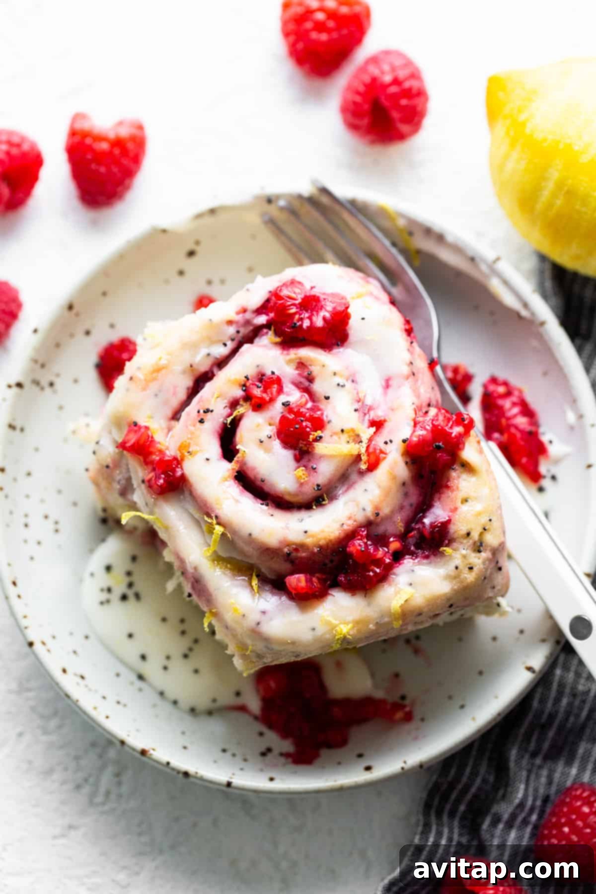 A single raspberry lemon poppy seed roll on a plate with a fork.