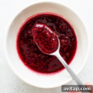Raspberry jam in a white bowl with a spoon.