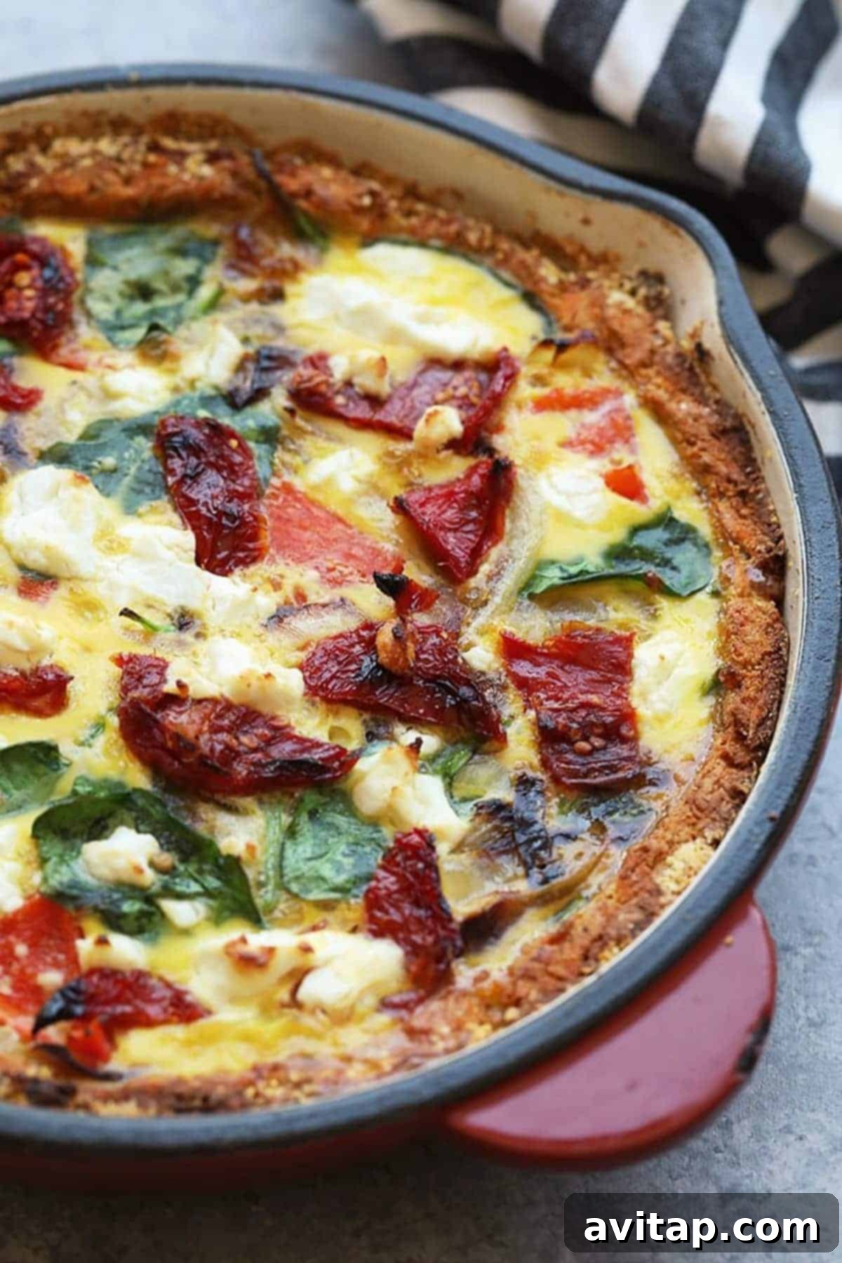 The March Wellness Culinary Club 6 A delectable slice of sweet potato crust quiche, generously filled with vibrant spinach and juicy tomatoes, beautifully presented in a rustic cast iron pan. A perfect example of a healthy, homemade, and satisfying meal from scratch, ideal for any occasion.