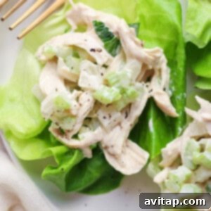 A chicken salad with creamy dressing served on a fresh lettuce leaf with a pair of gold forks on the side.