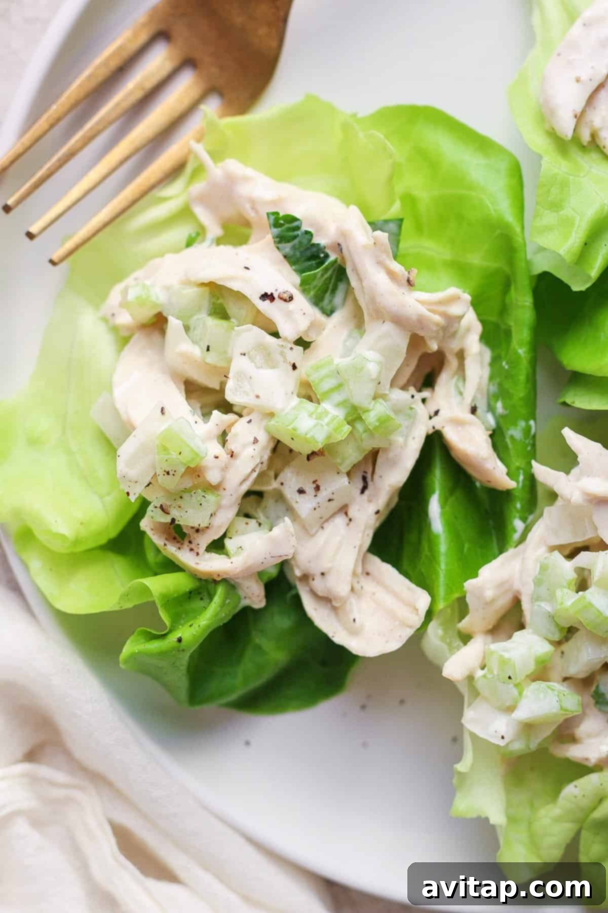 A chicken salad with creamy dressing served on a fresh lettuce leaf with a pair of gold forks on the side.