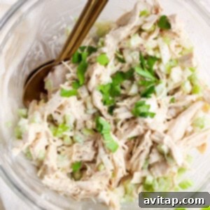 A bowl of shredded chicken salad garnished with chopped green onions and herbs.