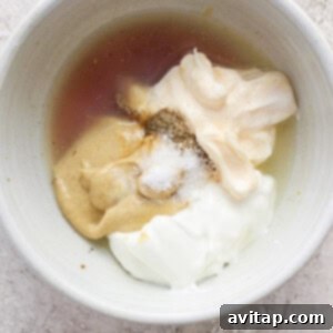 A bowl containing ingredients such as a liquid (possibly vanilla extract or a similar flavoring), spices, and creamy substances like mayonnaise, sour cream, or yogurt, with a sprinkling of fine.