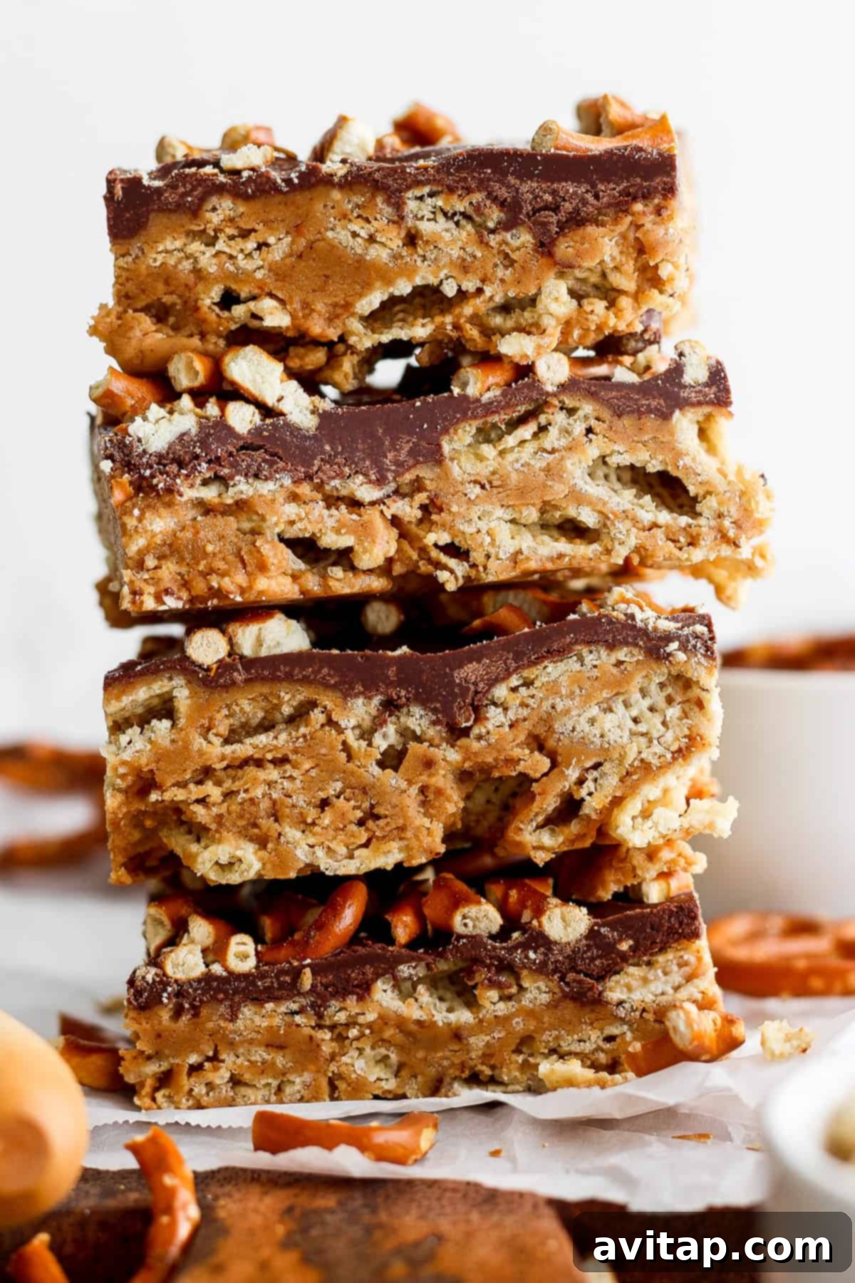 A stack of three layered peanut butter bars with a chocolate topping and crushed nuts on parchment paper.