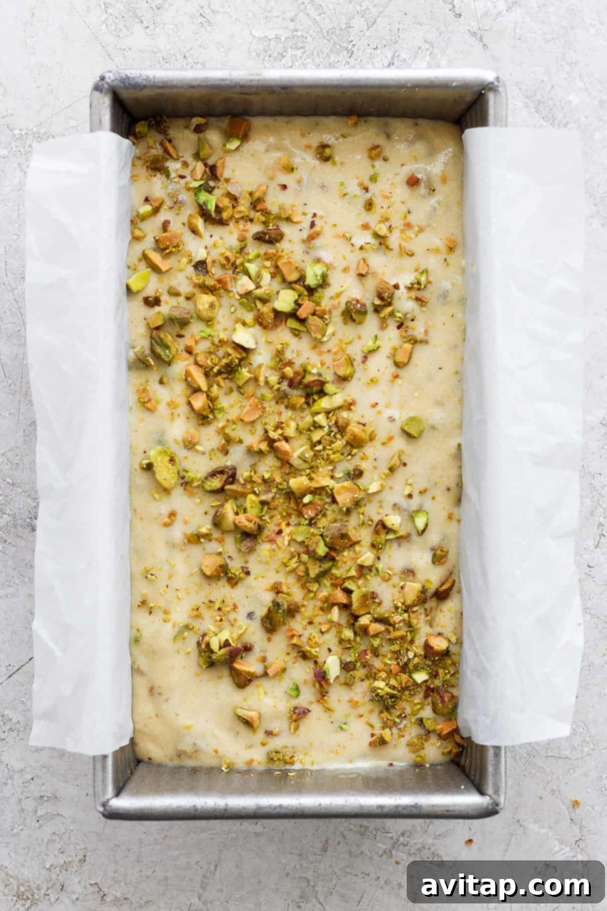 Unbaked dough in a metal tray topped with chopped nuts, prepared for baking and lined with parchment paper.