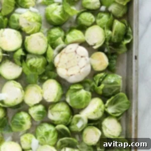 Brussels sprouts and garlic arranged in a single layer on a baking sheet, ready for the oven.
