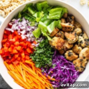 A white bowl filled with a mix of fresh asian chicken salad ingredients, tossed with dressing.
