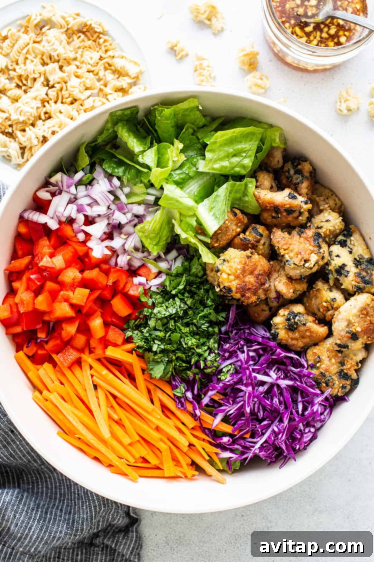 All the vibrant ingredients of the ramen noodle chicken salad, including fresh vegetables, crispy chicken, and toasted noodles, mixed in a large bowl.