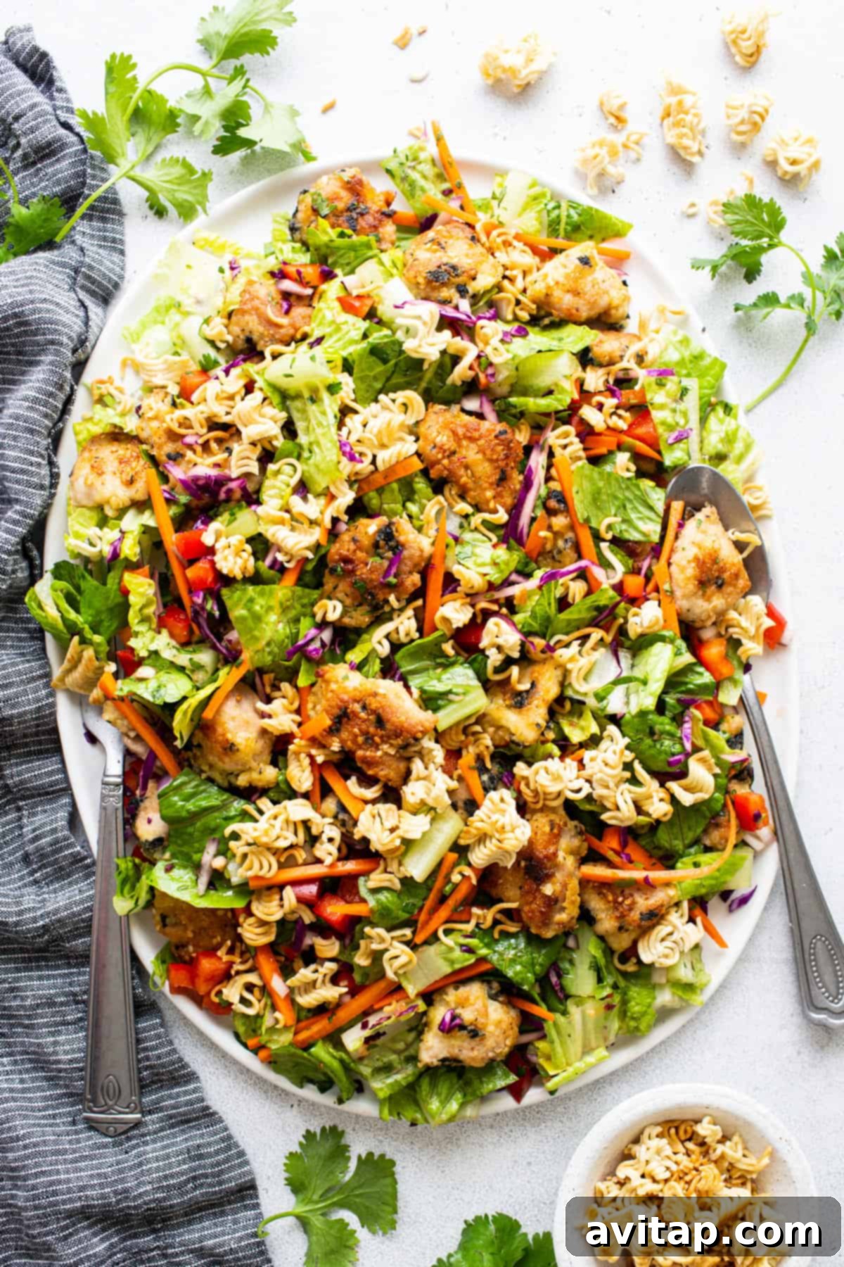 A beautifully presented Asian chicken noodle salad in a white bowl, garnished with fresh cilantro and sesame seeds.