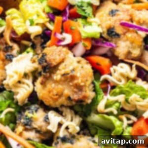 A bowl of Asian-inspired chicken noodle salad, featuring crispy chicken, fresh vegetables, and toasted ramen.