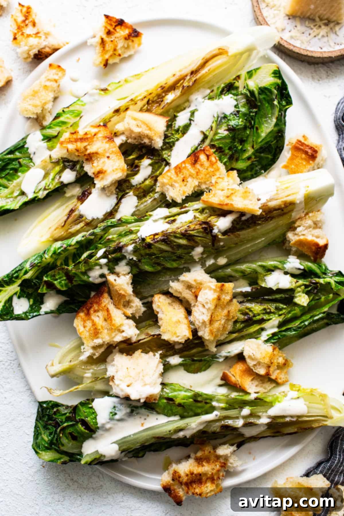 Flame-Kissed Caesar with Crispy Charred Croutons 6 A vibrant grilled romaine lettuce topped with golden croutons and generously drizzled with creamy dressing on a clean white plate.