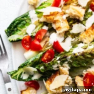 Flame-Kissed Caesar with Crispy Charred Croutons 11 Grilled caesar salad with chicken, cherry tomatoes, croutons, and shaved parmesan cheese on a white plate, beautifully presented.