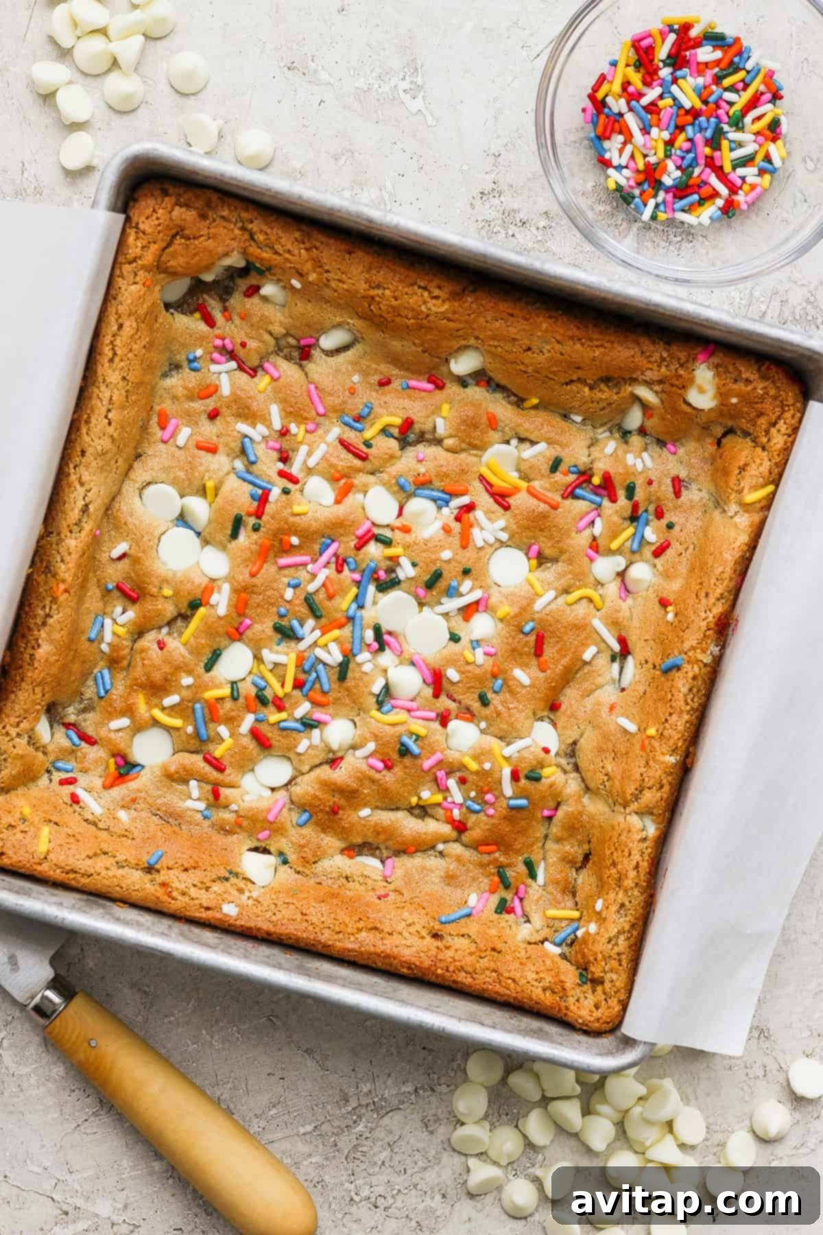 Freshly baked blondie bars, adorned with colorful sprinkles, cooling in a square baking pan.