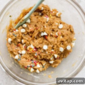 A bowl of cookie dough with sprinkles and a spoon, showcasing the well-mixed batter.