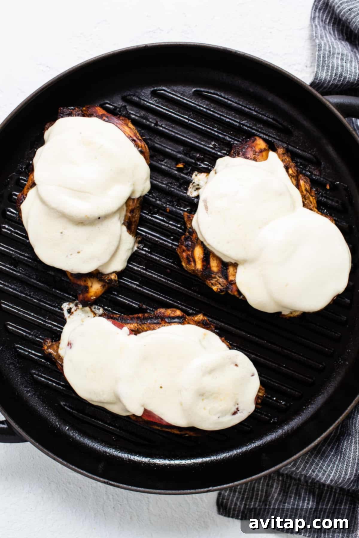 California Sunshine Grilled Chicken 4 Three grilled chicken breasts with sauce on a grill, showing the melting cheese and tomatoes during the grilling process.
