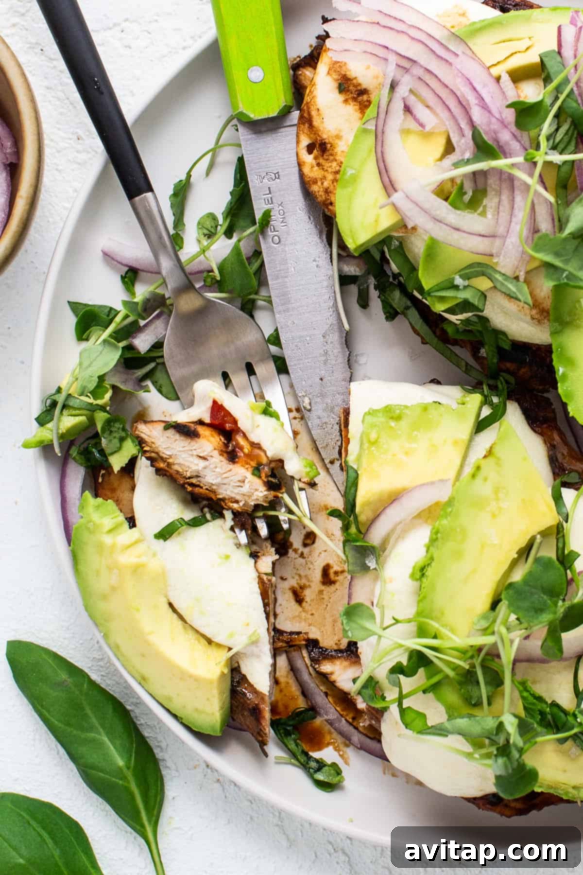 California Sunshine Grilled Chicken 5 A plate with grilled chicken and avocado on it, topped with basil, red onion, and microgreens, ready to be served.
