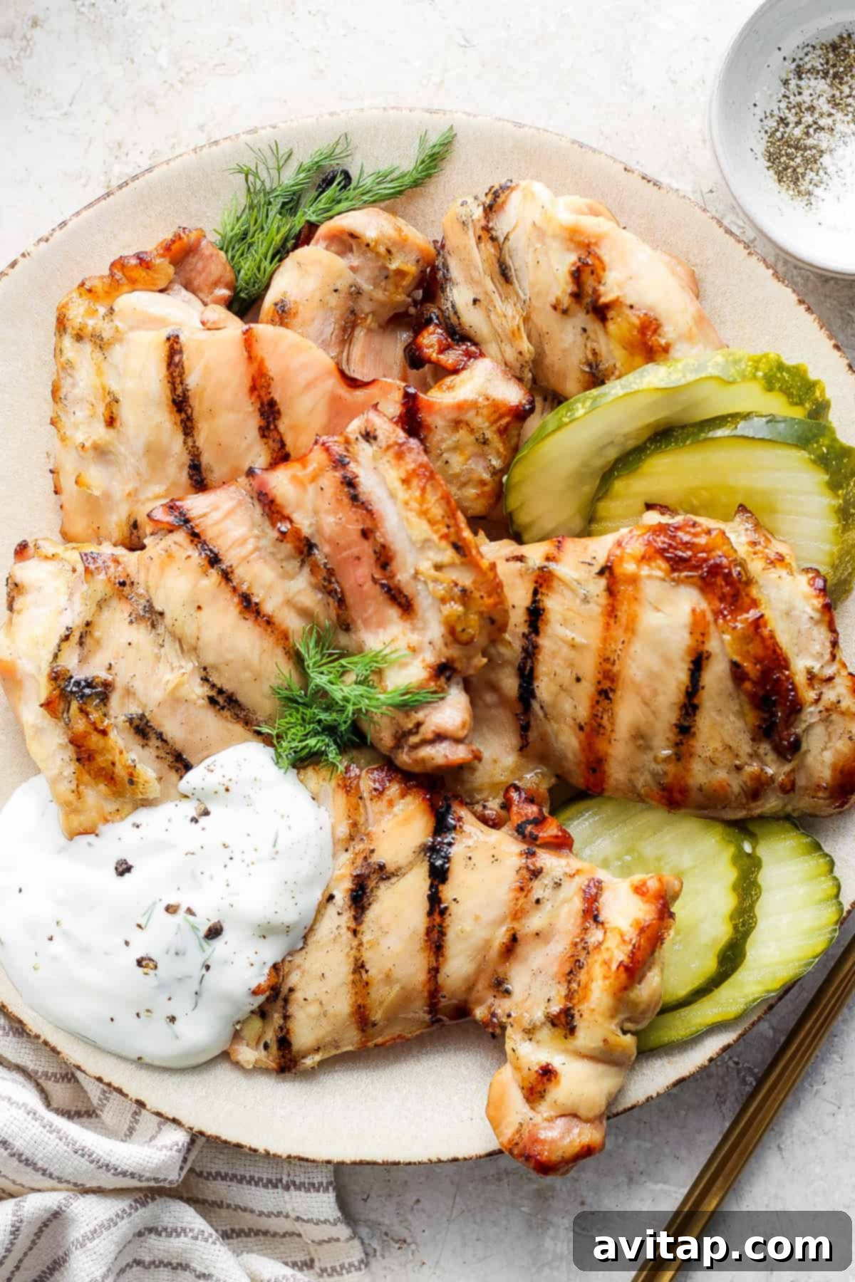 Grilled chicken breasts served with pickles and a dollop of sauce on a plate.
