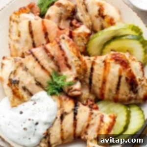 Grilled chicken breast slices served with pickles and a dollop of sour cream on a plate.