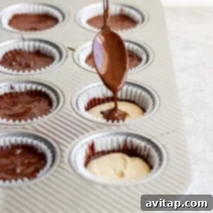 Drizzling chocolate over peanut butter in lined muffin cups using a spoon.