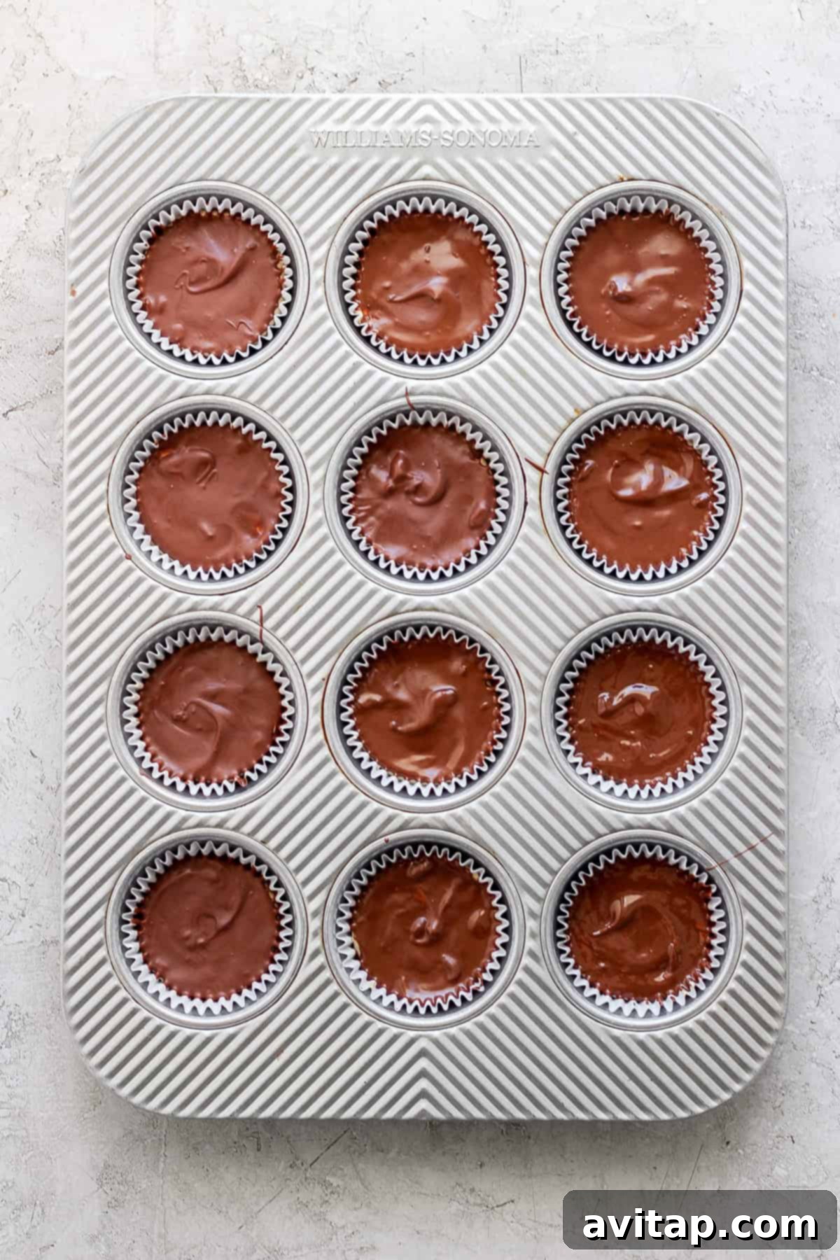 A tray of freshly baked chocolate muffins in paper liners, organized in a 4x3 grid, on a white textured surface.