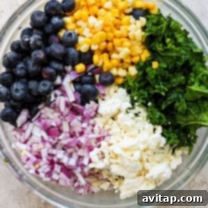 A colorful salad mixture in a bowl, featuring massaged kale, bright blueberries, crisp corn, chopped red onions, and crumbled feta cheese, perfectly combined for the protein bowl.