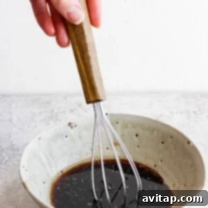 A hand expertly whisking a vibrant salad dressing mixture in a ceramic bowl, preparing to enhance the flavors of the kale salad with its sweet and tangy notes.