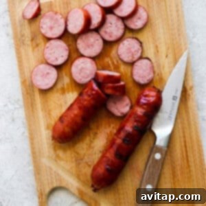 Perfectly sliced savory sausage rounds arranged on a rustic wooden cutting board next to a chef's knife, ready for inclusion in the protein bowl for a hearty and flavorful component.