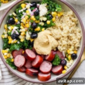 A beautifully assembled protein bowl with fluffy quinoa, perfectly sliced sausage, a colorful mix of massaged kale and fresh vegetables, and a creamy dollop of hummus, ready to be enjoyed.