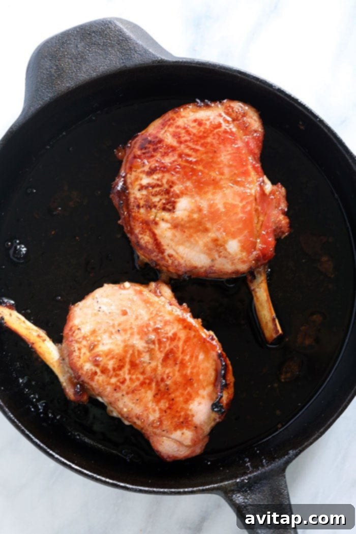 two beautifully cooked bone-in pork chops in a cast iron skillet