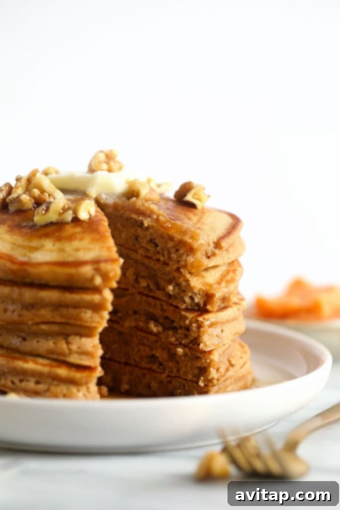 A stack of golden brown sweet potato pancakes drizzled with maple syrup on a white plate, ready to be enjoyed.