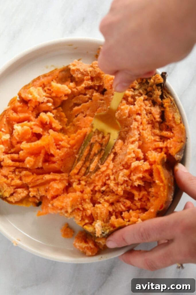 A peeled, cooked sweet potato being mashed into a smooth puree in a bowl.