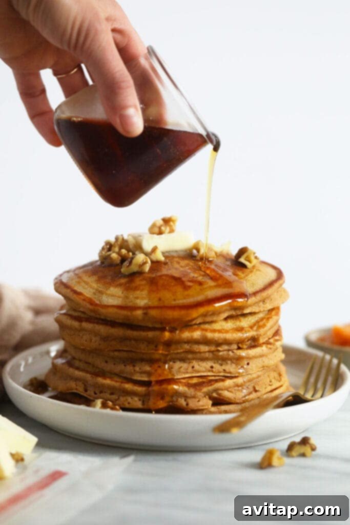 Close-up of golden sweet potato pancakes being drenched in rich maple syrup.
