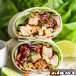 A close-up of a chicken wrap sliced in half, filled with diced chicken, purple cabbage, carrots, lettuce, and peanuts, displayed against a fresh, green backdrop.