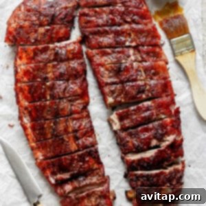 Two racks of barbecued ribs cut into portions, placed on parchment paper with a knife, a brush, and a bowl of sauce.
