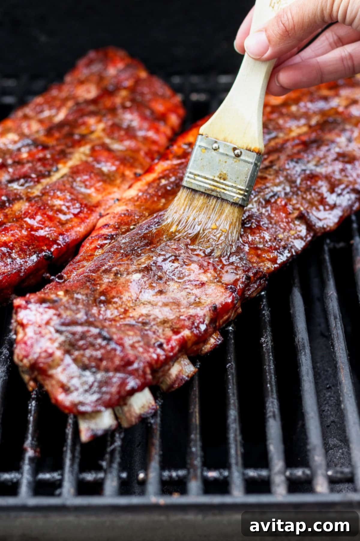 Glazed ribs on the grill, with a basting brush in action, creating a sticky, caramelized coating.