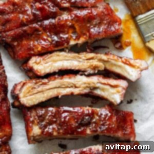 Close-up view of several pieces of glazed, barbecued ribs on parchment paper, with a brush coated in sauce to the side.