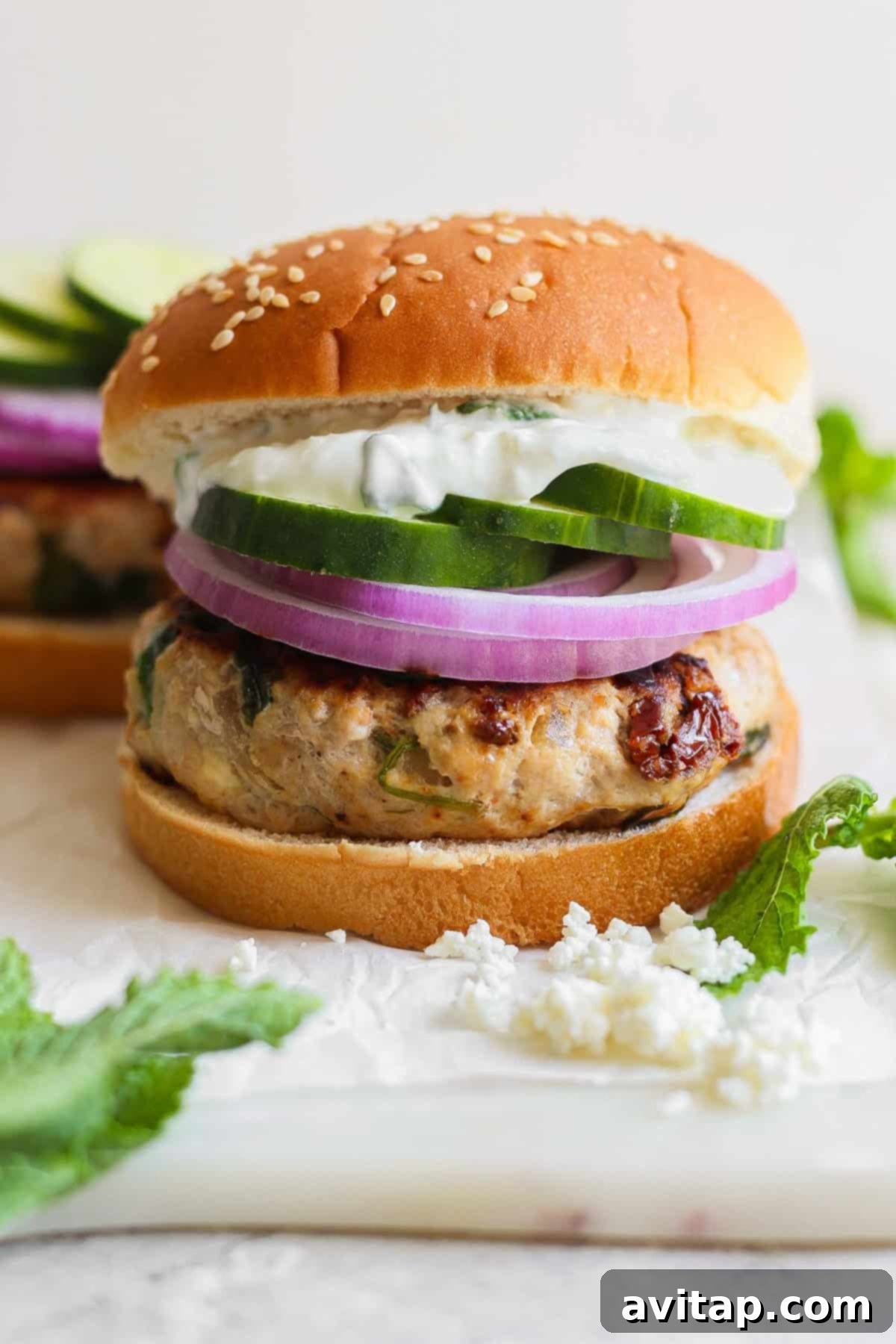 A perfectly assembled Mediterranean burger with tzatziki sauce, sliced cucumbers, and red onions.