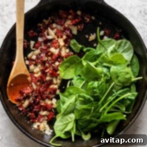 Fresh spinach wilting in a skillet with sautéed onions and garlic.