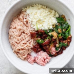 Hands mixing ground chicken, ground pork, cooked spinach, sun-dried tomatoes, and feta cheese in a bowl.