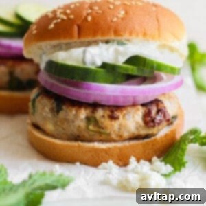 A fully assembled Mediterranean burger on a bun with tzatziki, red onion, and cucumber.