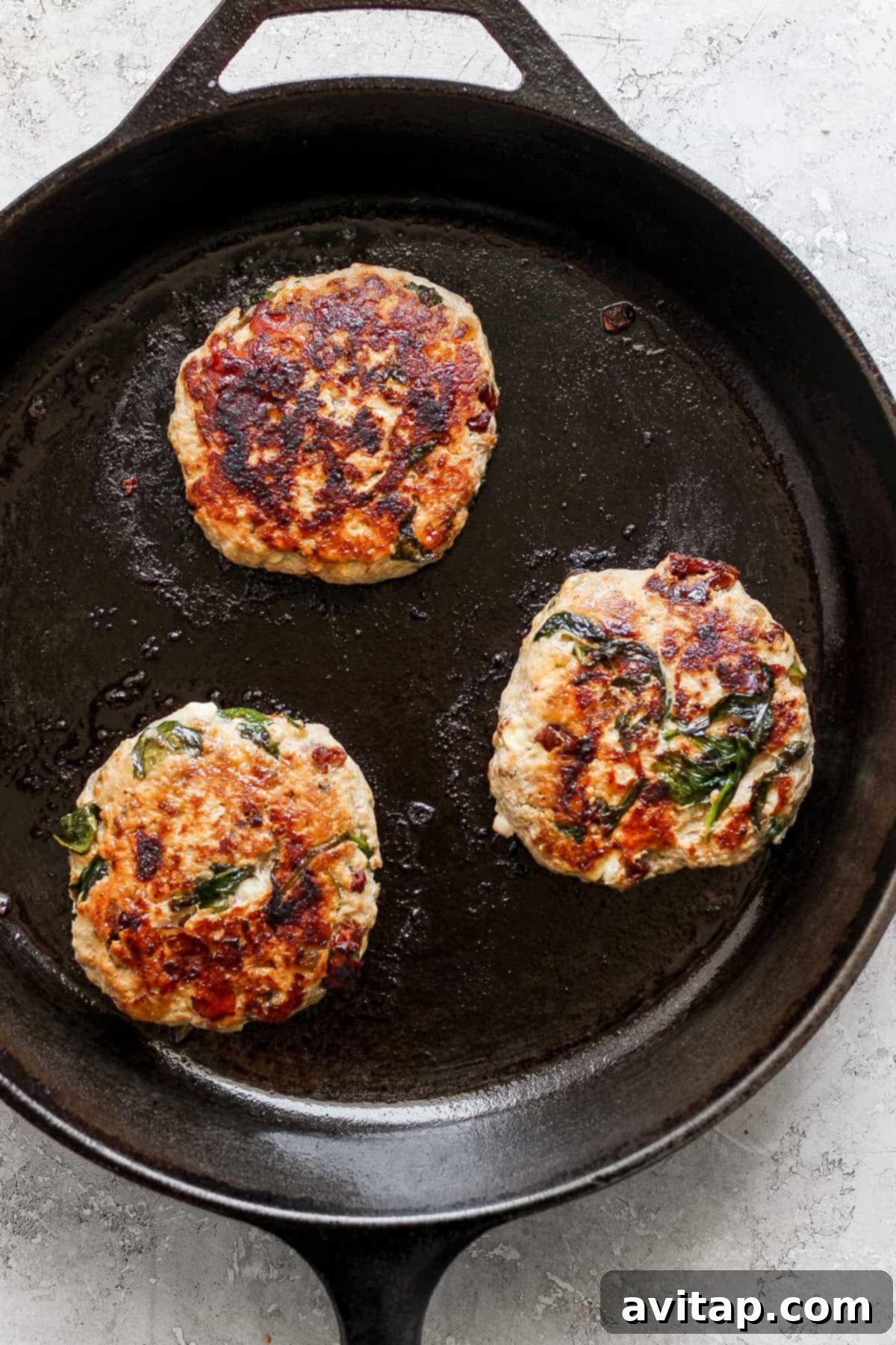 A close-up shot of a Mediterranean burger patty sizzling in a hot cast iron pan.