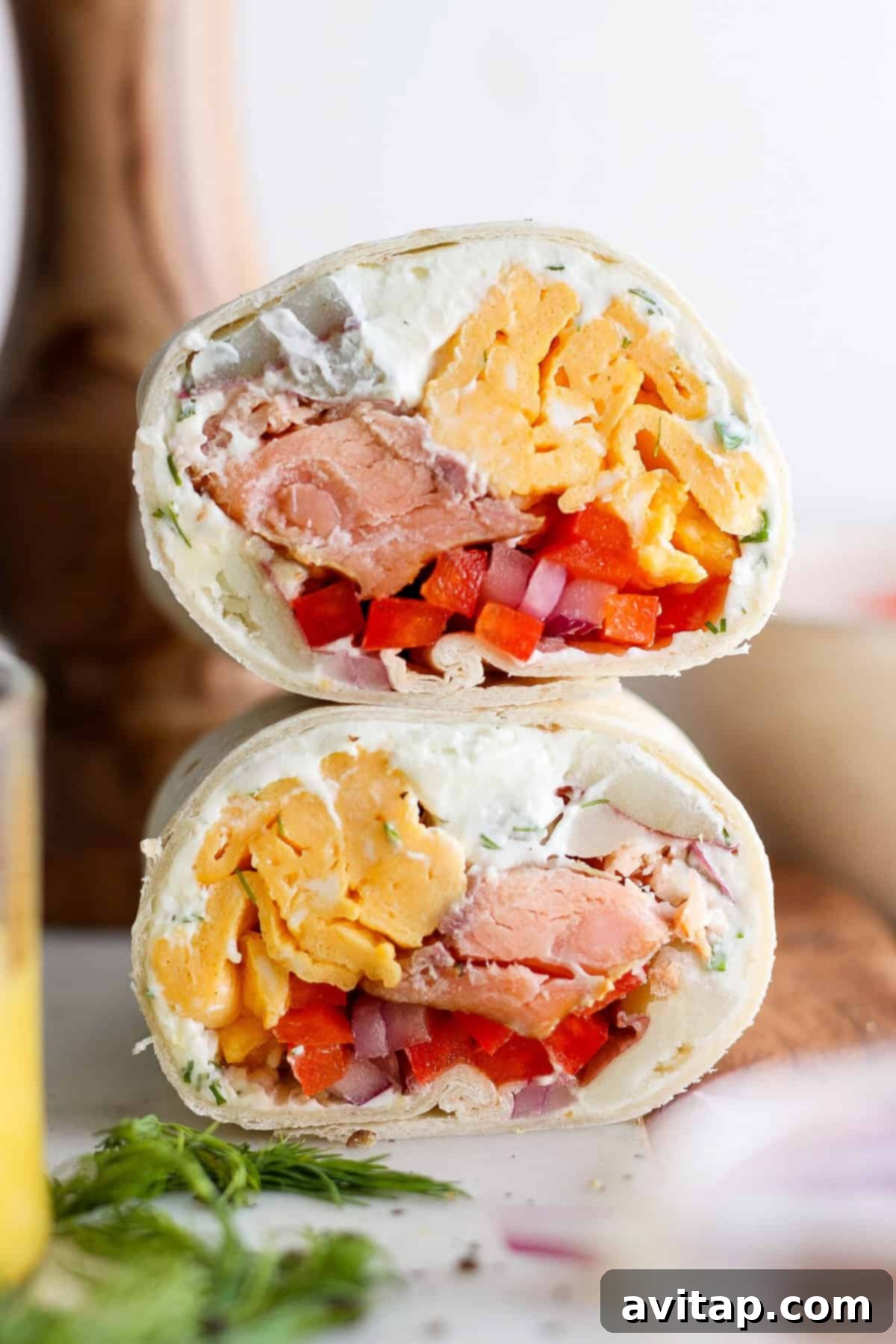 A perfectly rolled smoked salmon breakfast burrito, sliced in half to reveal layers of scrambled eggs, smoked salmon, potatoes, and herb cream cheese, resting on a white plate.