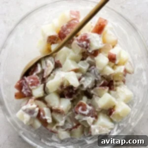 A bowl of potato salad with diced potatoes, creamy dressing, and fresh herbs, served with a wooden spoon.