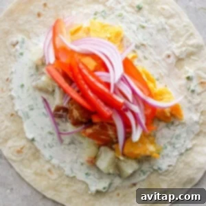 A flour tortilla layered with herb cream cheese, red bell pepper, red onion, and other ingredients, before rolling.
